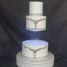 a three tiered wedding cake with white frosting and silver decorations on top, sitting on a pedestal