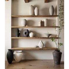 several vases are arranged on wooden shelves in a room with white walls and wood flooring