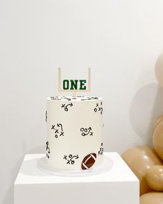 a football themed birthday cake sits on a pedestal with balloons in the background and one sign