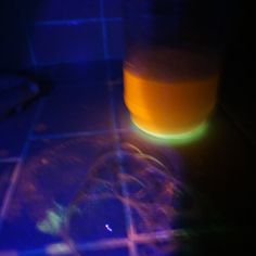 a glass filled with liquid sitting on top of a tiled floor next to a blue light