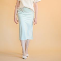 a woman in a white shirt and light blue skirt is standing against a beige background