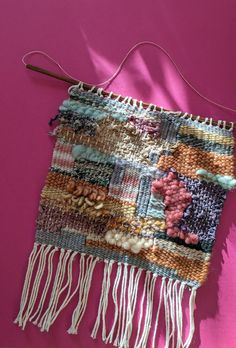 a woven piece with tassels hanging on a pink wall