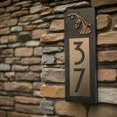 a house number sign mounted to the side of a stone wall with a brick building in the background