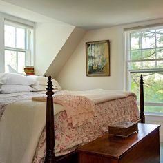 a bed sitting under two windows next to a wooden table and chair in a bedroom