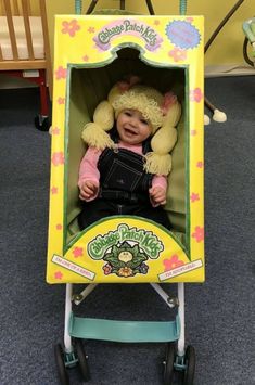 a baby sitting in a toy stroller with its head turned to look like she's smiling