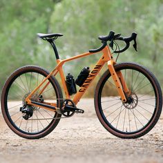 an orange and black bike parked on the side of a dirt road in front of trees