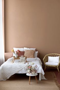 a bed with white sheets and pillows in a bedroom next to a chair, table and window