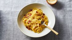 a white bowl filled with pasta and bacon on top of a table next to an orange slice