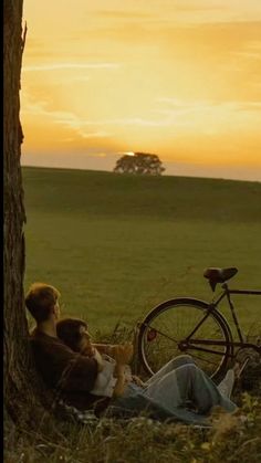 two people sitting under a tree with a bike in the background