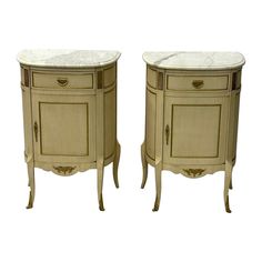 two white marble topped nightstands side by side on stands, one with doors open and the other closed