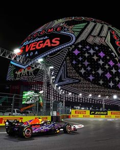 a red bull racing car driving down a race track at night with the las vegas sign in the background