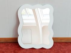 a white mirror sitting on top of a red carpeted floor next to a window