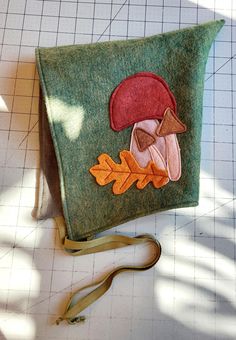 a green bag with an embroidered mushroom on the front and orange leaves on the back