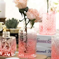 pink glass vases with roses in them sitting on a table next to other items