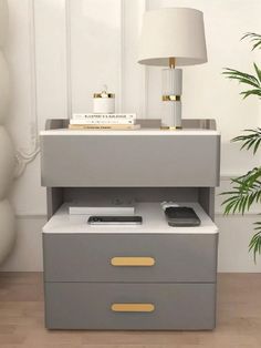 a nightstand with a lamp and some books on it next to a potted plant