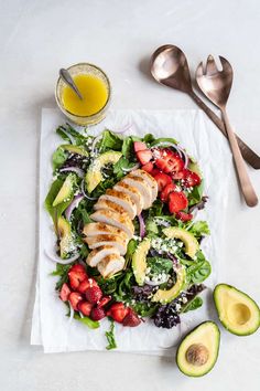 a salad with chicken, strawberries, avocado and dressing next to two spoons