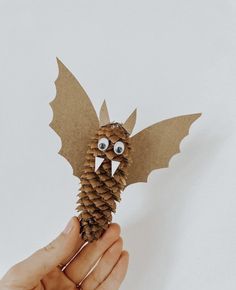 a hand holding a pine cone shaped like a bat with eyes and wings on it