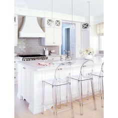 a white kitchen with four clear chairs and an island in front of the countertop