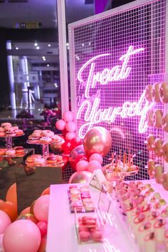 pink and gold desserts on display in front of a neon sign that says treat yourself