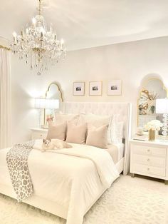 a white bedroom with a chandelier hanging from the ceiling and pillows on the bed