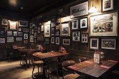 an empty restaurant with many framed pictures on the wall and wooden tables in front of them