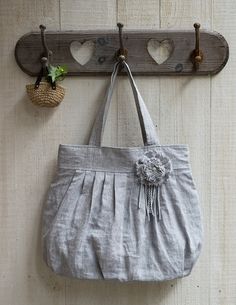 a gray purse hanging on a wall with two hooks and a plant in the corner