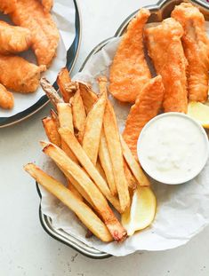 two plates filled with fried fish and fries next to dipping sauce on top of them