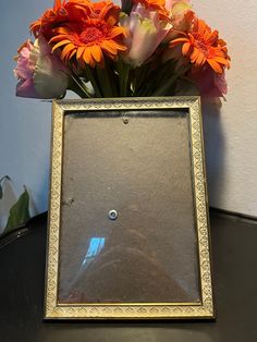 a vase filled with orange and pink flowers on top of a black table next to a white wall