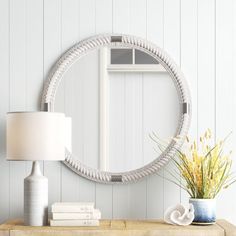 a table with a lamp, vase and mirror on it in front of a white wall