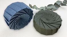 an origami box and a paper flower on a white surface with green leaves