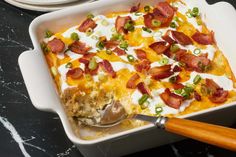 a casserole dish with bacon, green onions and sour cream on the side