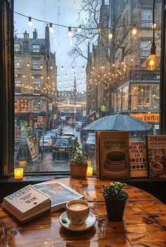 a cup of coffee sitting on top of a wooden table next to a window covered in lights