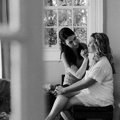 two women sitting next to each other in front of a window, one brushing her teeth