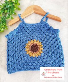 a blue crocheted top with a sunflower on it and a wooden hanger