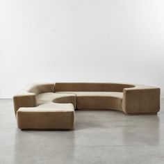 a curved couch sitting on top of a cement floor next to a white wall in an empty room