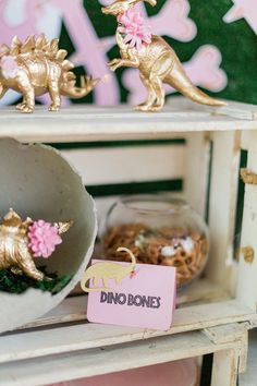 some gold dinosaurs are on top of a white shelf with pink and yellow tags in front of them