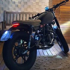 a black motorcycle parked on top of a wooden floor next to a wall with lights