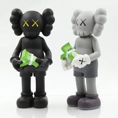 two black and white figurines with yellow crosses on their faces, one holding a green box