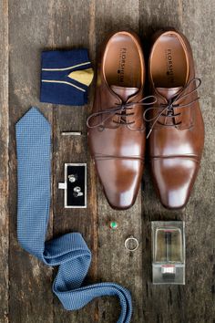 a pair of brown shoes, tie, and other items laid out on a wooden surface