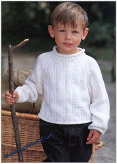 a young boy in a white sweater holding a stick and looking at the camera while standing next to a wicker basket