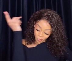 a woman with long curly hair is making the peace sign while standing in front of a black curtain