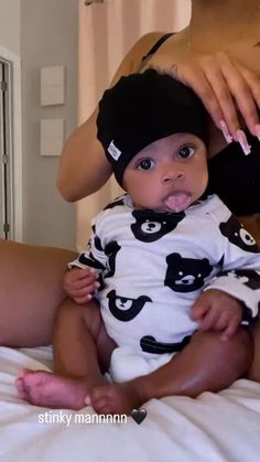 a woman brushing her baby's teeth while sitting on the bed in front of him