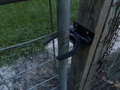 a metal fence with a hook attached to it and some grass in the back ground