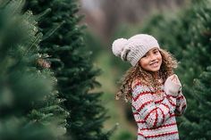 a woman standing in between rows of christmas trees