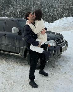 a man and woman are kissing in front of a car on the snow covered ground