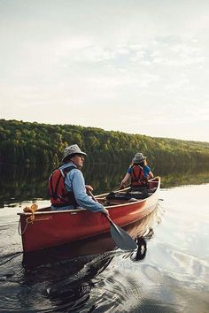 two people in a red canoe paddling on the water with trees in the background