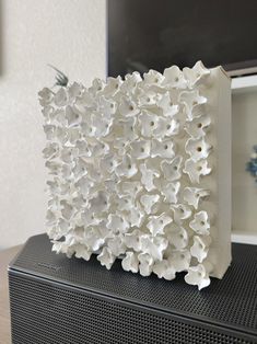 a white sculpture is sitting on top of a black speaker with flowers in it's center