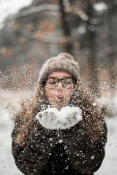 a woman standing in the snow with her hands up to her face and looking at the camera