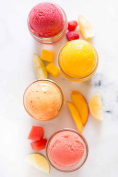 three glasses filled with different colored ice creams and slices of fruit next to each other