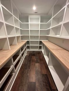 an empty walk in closet with white shelving and wood flooring on the walls